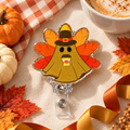 Gold-tone glitter ghost badge reel with a pilgrim-style hat, yellow orange and red turkey feathers, and a tiny pumpkin coffee cup.