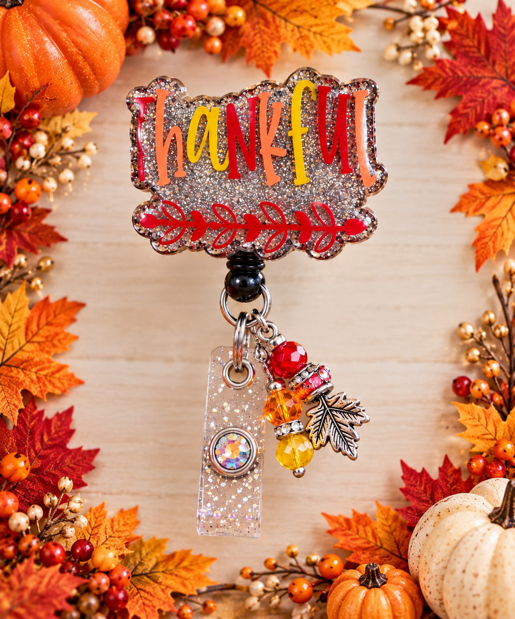 Silver-toned glitter Thankful badge reel with red leafy artwork in an autumn display