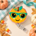 Smiling orange pumpkin badge reel with teal glasses, teal leaf, glittery border, and clear snap strap