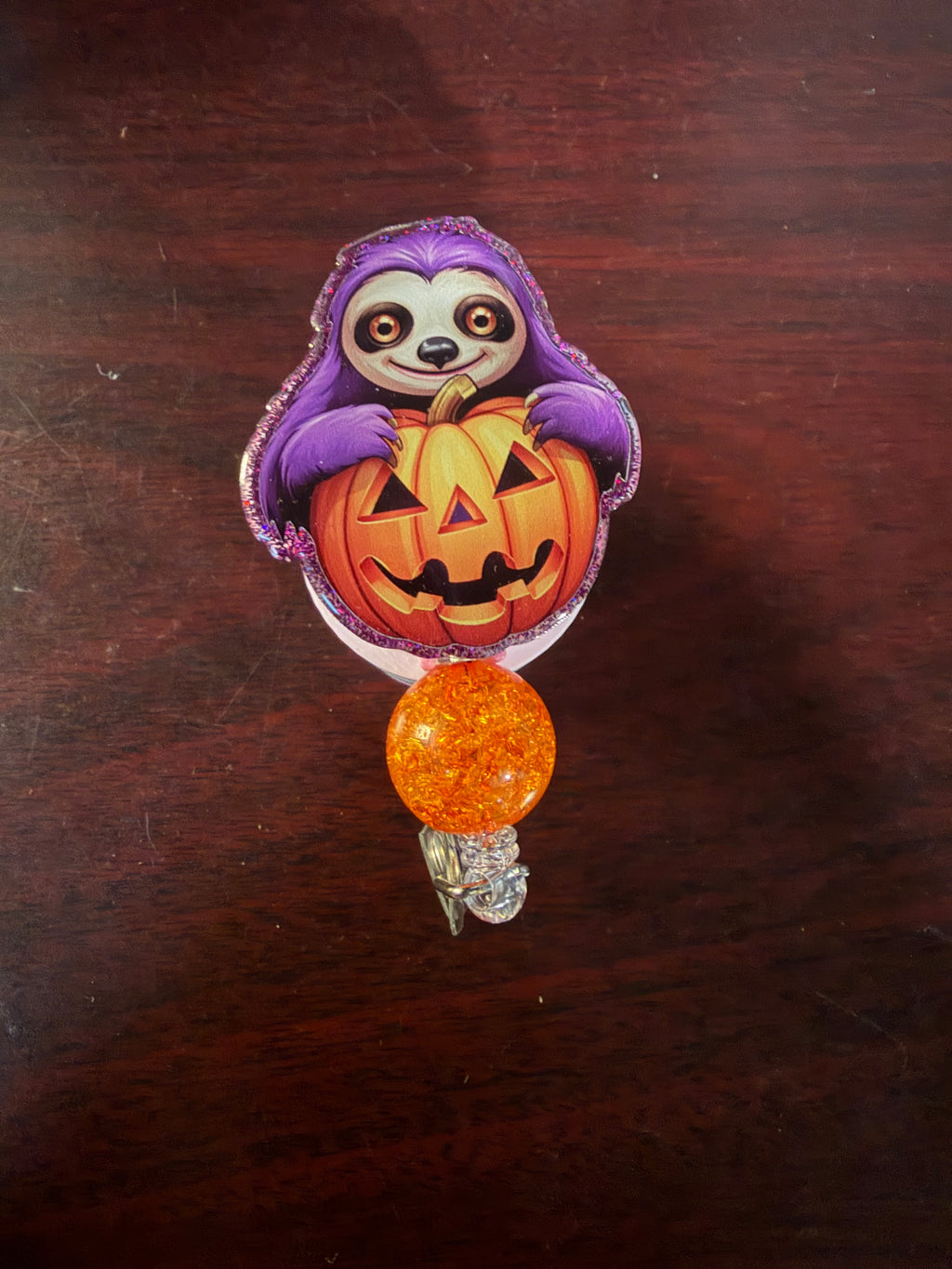 Purple sloth hugging a jack-o-lantern glitter acrylic badge reel on a dark wood background