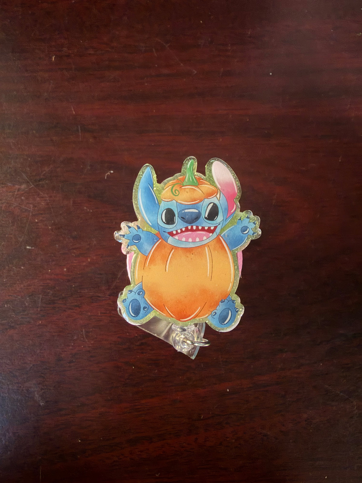 Stitch pumpkin glitter acrylic badge reel on a dark wood background