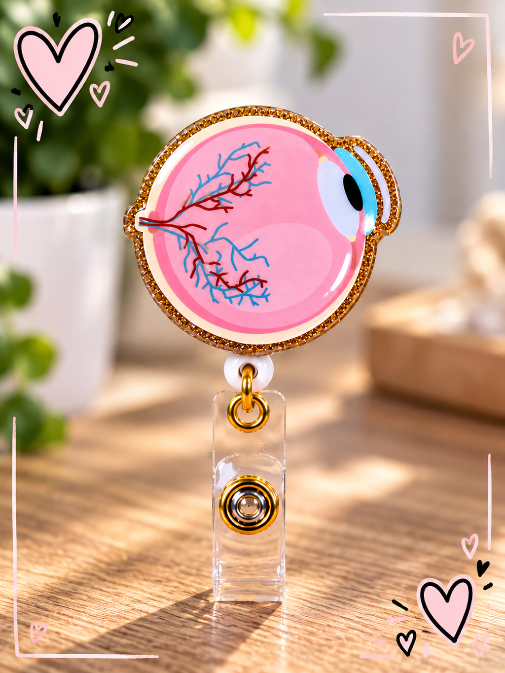 Pink anatomical eye badge reel with glittery gold-tone border and clear snap strap